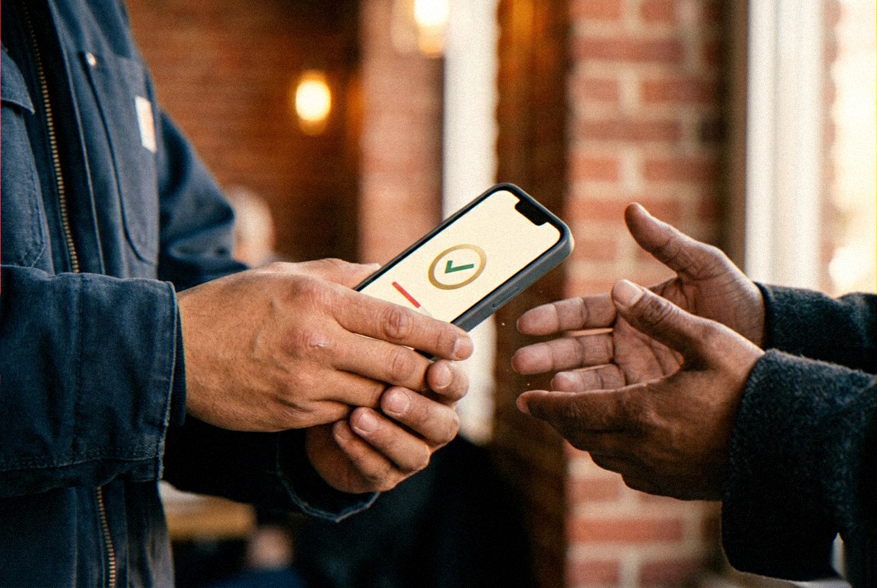 Client and freelancer confirming a gig on their phones outside a brick Pittsburgh cafe.